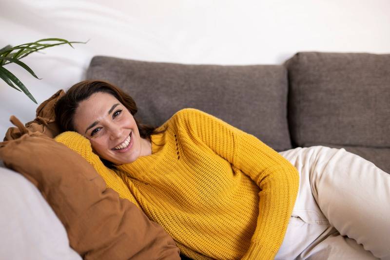 Happy young woman relaxing on a pillow at home and looking at camera. Portrait of cheerful beautiful girl in relaxing and resting on sofa.
