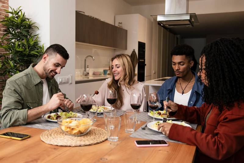Carefree young people eating and drinking on a modern apartment. Diverse group of relaxed friends having party diner at home. 