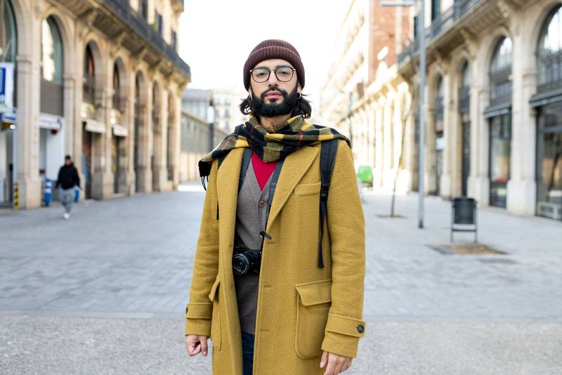 Young tourist with beard standing at the city looking at camera. Front view of a hipster male in Barcelona. Travel concept. 