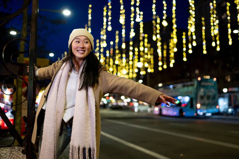 Happy young girl enjoying christmas lights in the street. Beautiful woman having fun at night in the city during winter.
