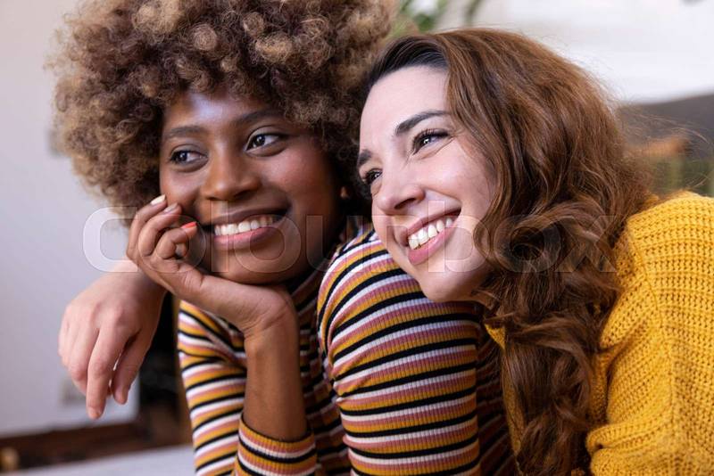 Close up of a beautiful multiracial couple hugging and relaxing. Portrait of two multiethnic smiling young women cuddling.
