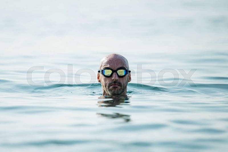 Confident man swimming in the ocean wearing glasses looking at camera. Swimmer pulling his head out of the water focused.