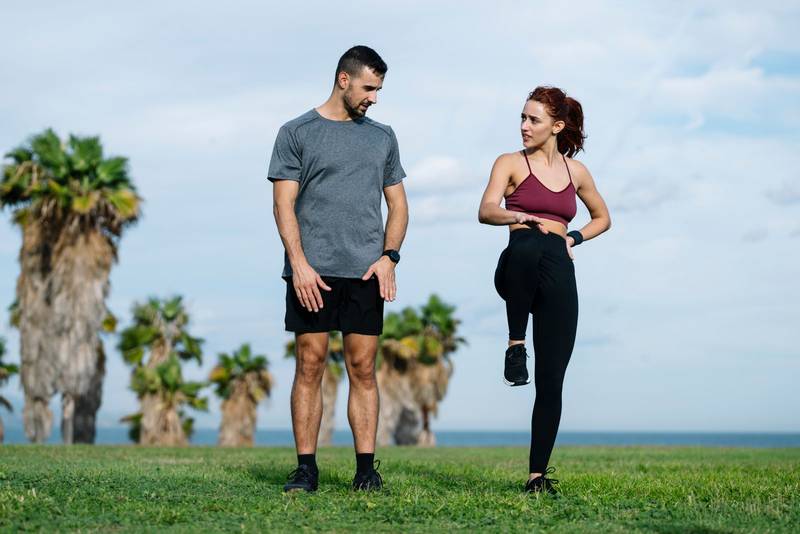 Athletic male looking at female coach in sportswear training workout outside. Lovely young adult couple warming up in park after running together. 