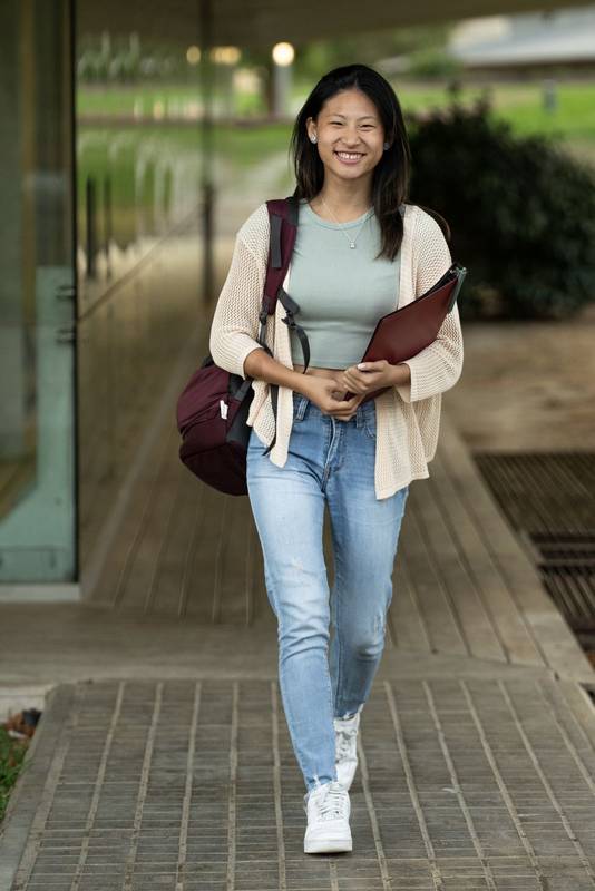 Handsome satisfied student walking outside holding a notebook looking at camera. Relaxed and happy woman standing outside with files on her hands.
