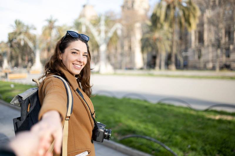 happy young woman tourist walking on the city and looking back - pov cheerful couple on holidays - travel, relaxation, friendship concept
