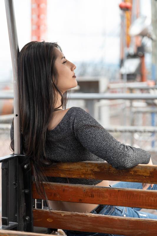 sitting on a wooden bench with her face in profile, relaxed resting in a park outdoors, lifestyle