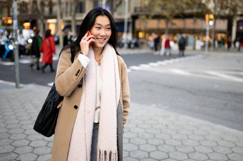 Beautiful young woman using her phone in the street. Happy confident woman having a call walking outside.