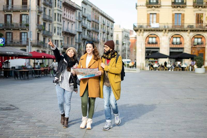 Group of tourists looking a map walking on the street. Three cheerful friends seraching a monument during a city travel