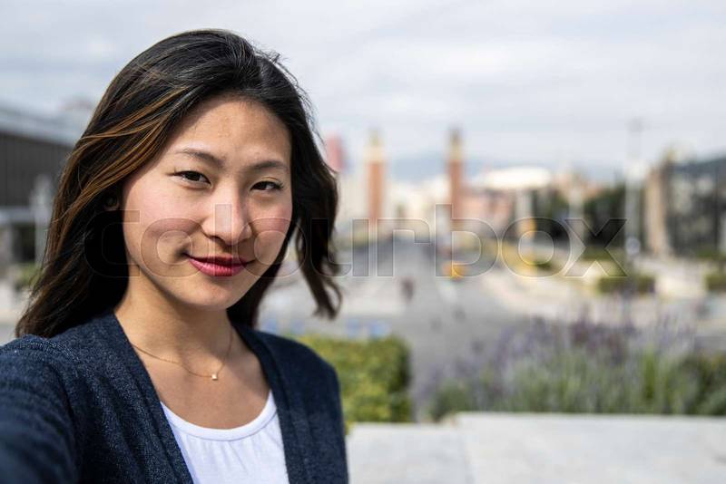 Confident handsome woman smiling relaxed and looking at camera in the street taking a selfie. Relaxed determined lady staring and holding the camera standing outdoors.