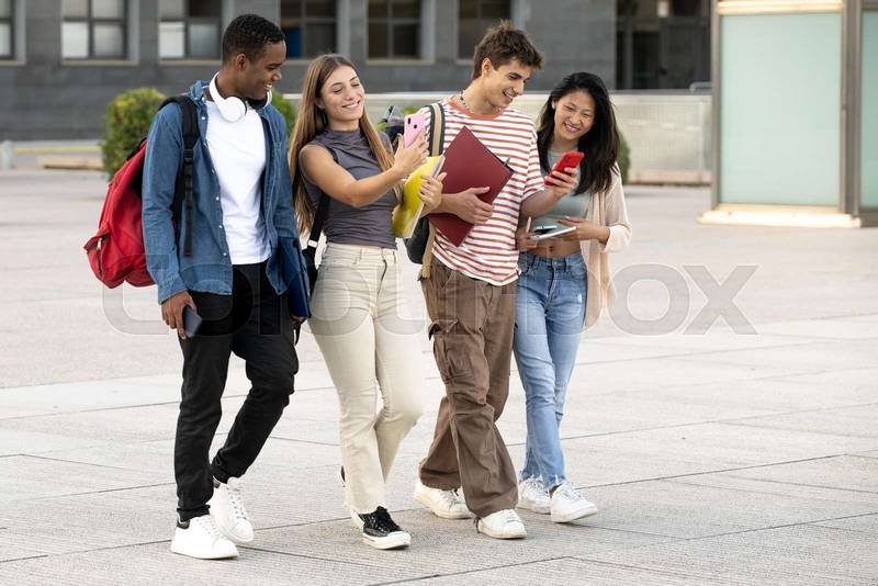 Young group of students walking and using phones in the street. Diverse students texting and laughing while moving in the campus.