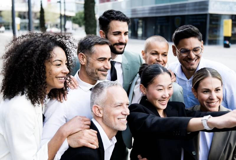 Multiracial group of successful business people taking a selfie outside. Diverse office colleagues taking a picture together smiling and bonding in the street.