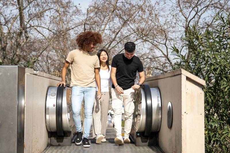 Diverse group of friends going up an outdoor escalator in a park. Three happy young people smiling and looking relaxed climbing up the stairs in the street.