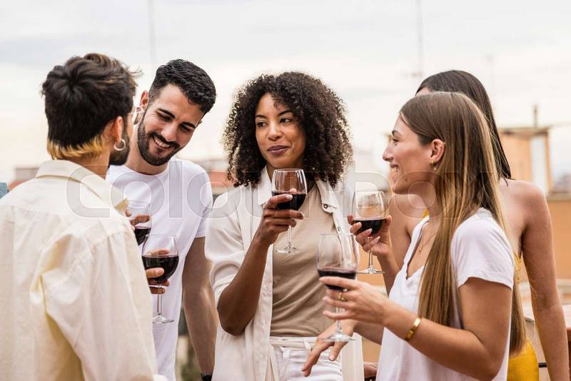 Multiracial group of friends having drinks standing in a rooftop party.Diverse young happy group of millennials having fun in a terrace.