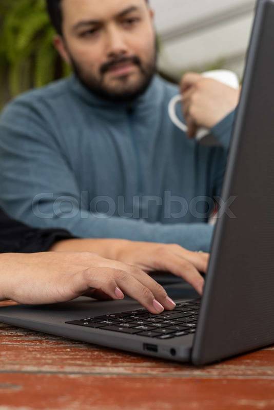 Man in blue works on laptop as colleague writes beside him, symbolizing collaboration