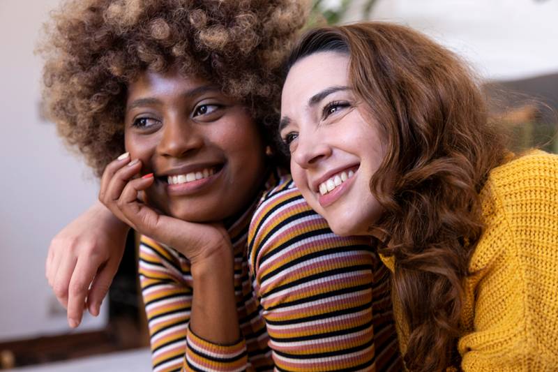 Close up of a beautiful multiracial couple hugging and relaxing. Portrait of two multiethnic smiling young women cuddling.