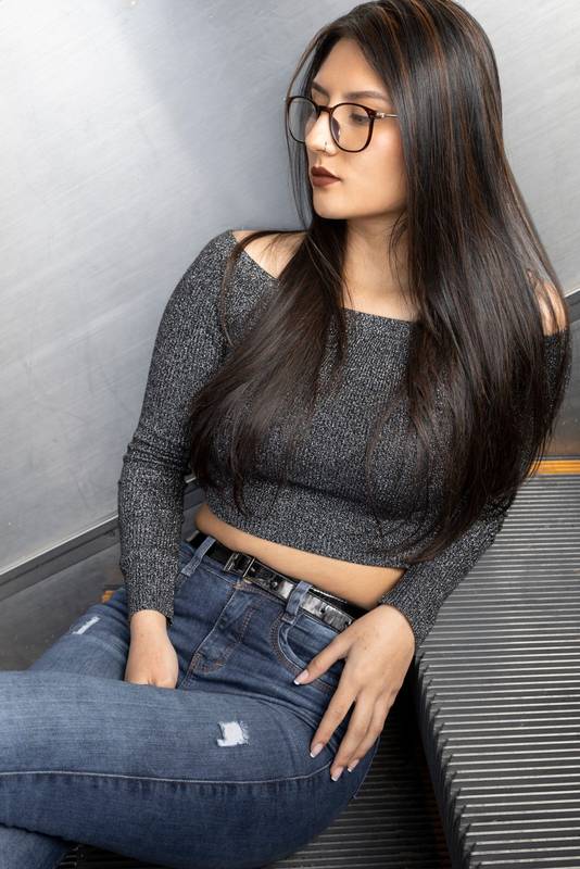 female model with straight black hair wearing glasses, jeans and a gray casual top, is resting