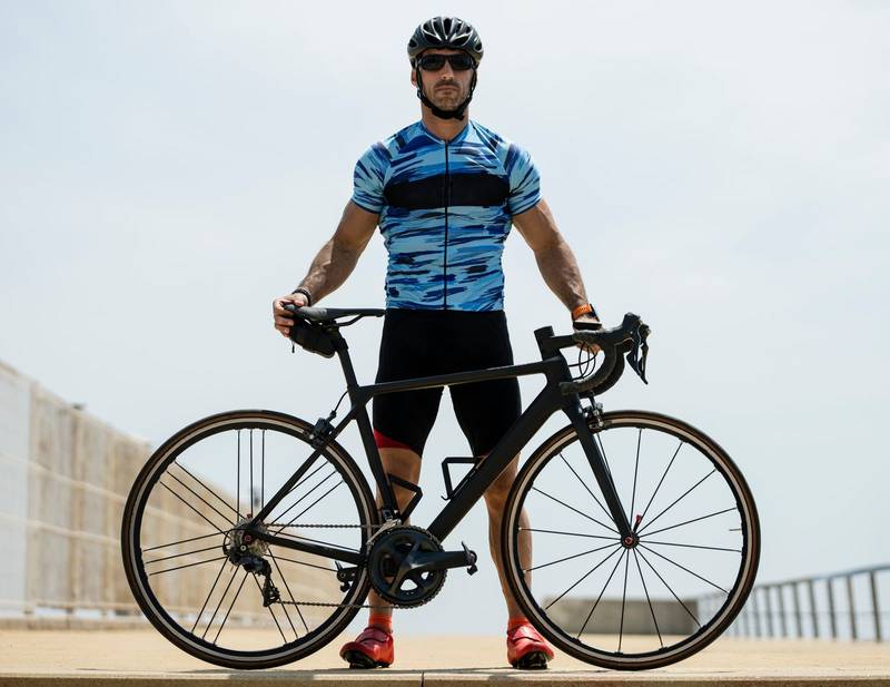 Athletic man holding a cycle wearing helmet and sunglasses outside. Cyclist standing with a bike wearing sport clothes in the street.