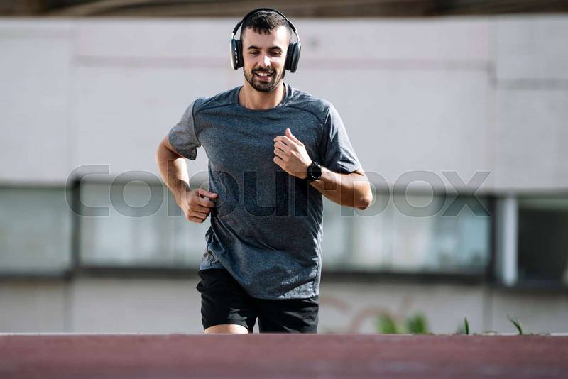 Sport fit man running wearing headphones outside. Young male athlete listening music during fitness training.
