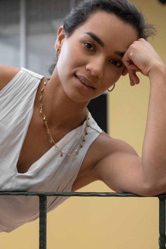 young brunette woman with her hair in a ponytail, wearing a necklace and earrings looking at the camera