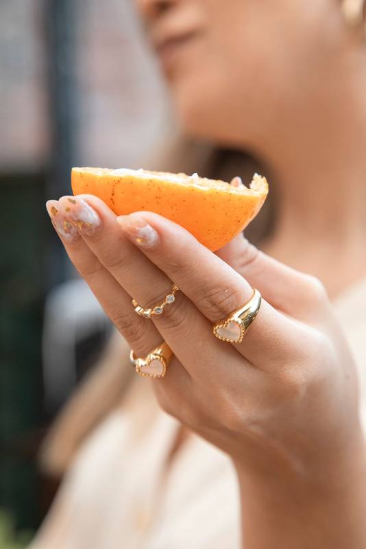 hand holding a piece of orange, wear various gold rings, modern jewelry and studio lifestyle