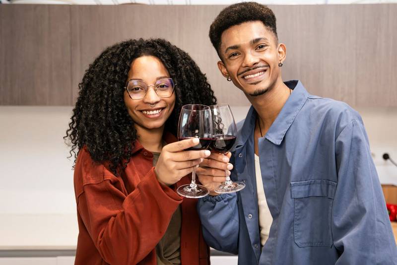 Happy young man and woman drinking with glasses in home. Cheering diverse couple toasting with wine in kitchen.