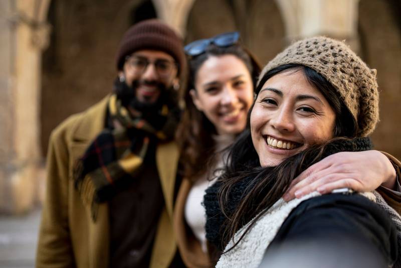 group of happy friends making a selfie in the street, focus on girl. three cheerful travelers taking a photo on their holidays. toursit concept.