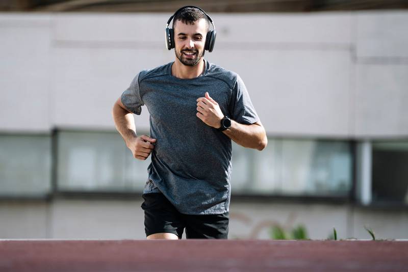 Sport fit man running wearing headphones outside. Young male athlete listening music during fitness training.