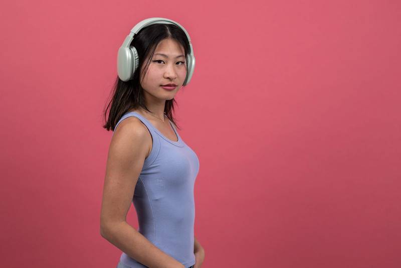 Confident woman with headphones looking to the camera. Proud young female listening to music isolated on a red background.