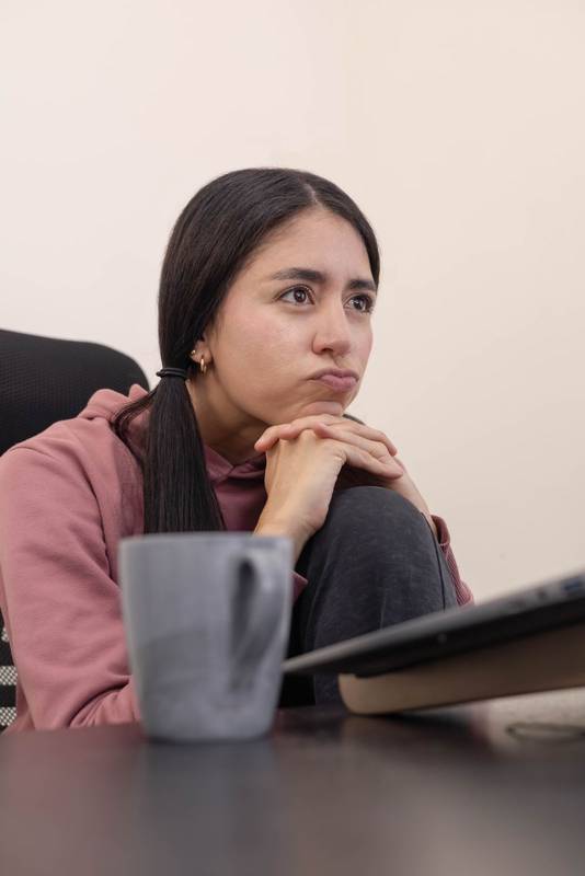 woman at her office desk gazes at her laptop screen with boredom, showing a lack of engagement while performing daily professional