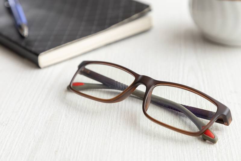 glasses on a wooden desk in the day, next to a notebook with a pen
