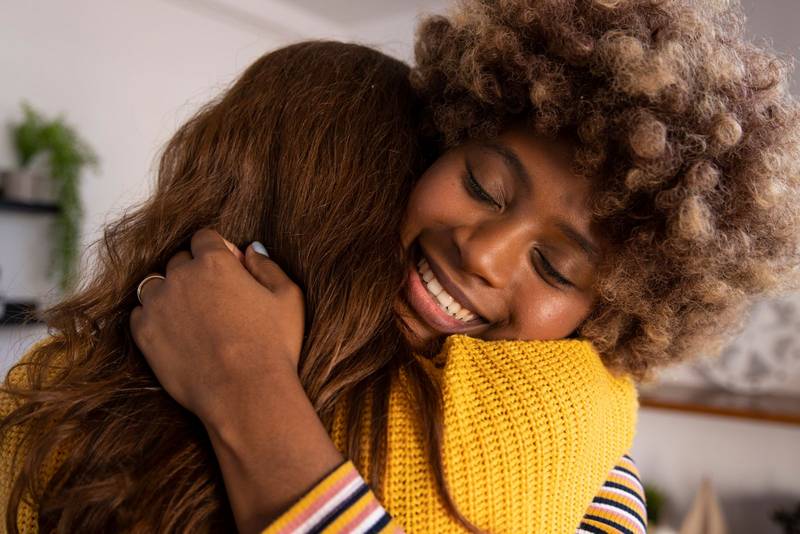 Carefree and joyful female couple hugging each other at home. Head shot close up happy multiracial girl cuddling smiling female friend.