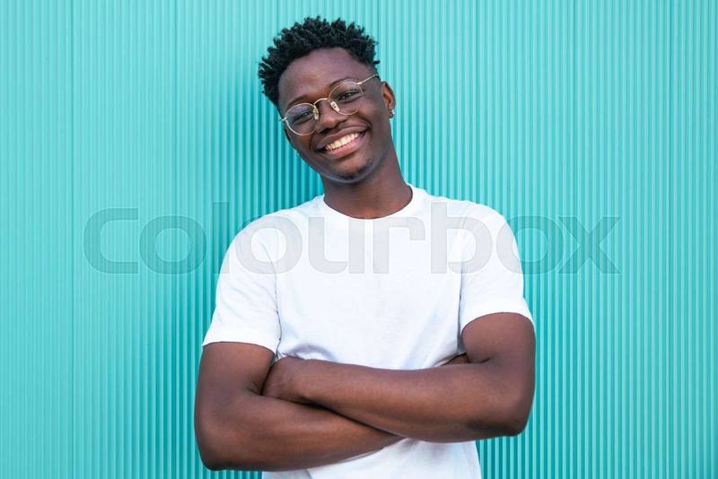 Happy young african american man smiling with arms crossed on turquoise background - Portrait of a cheerful young man - Happines and positive concept