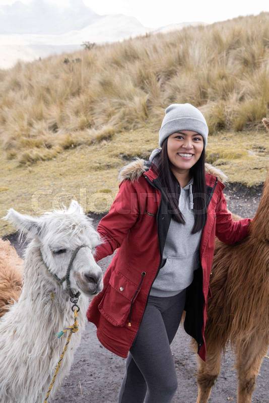 young woman wearing a wool cap and jacket next to llamas, mammal domestic animal, nature