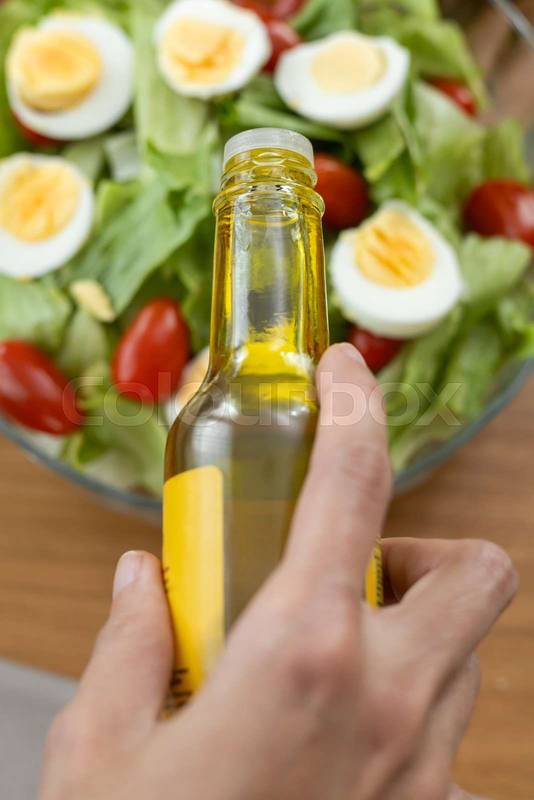 fresh salad with tomato, lettuce, and hard-boiled egg, being drizzled with olive oil from a bottle