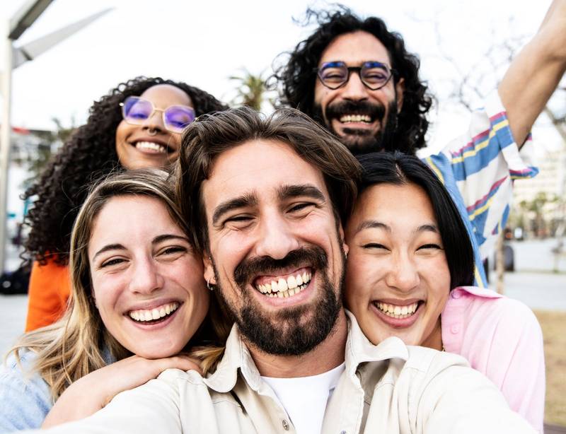 Close up of a diverse group of friends smiling and taking a selfie in the street. Cheerful multiracial group of young hipsters taking a picture outside and looking at camera.