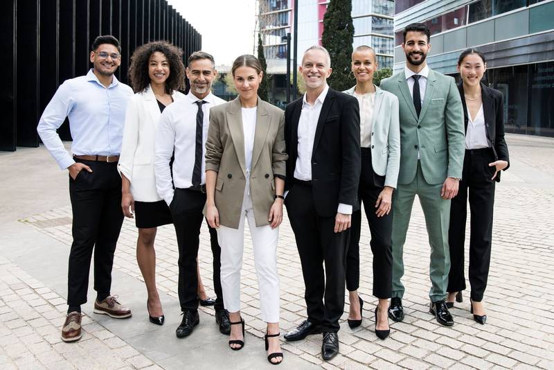 Group of smiling multiethnic businessman and businesswoman staring at camera outside. Multiracial cheerful confident executive team standing in the street.