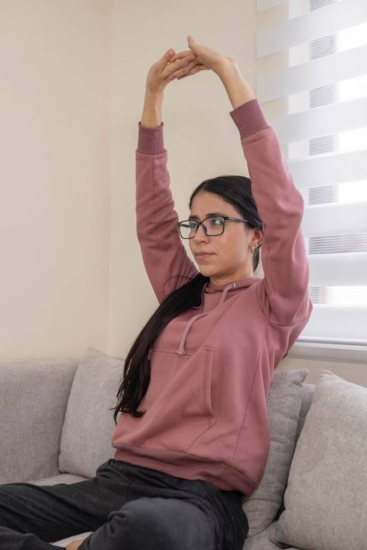 raising her arms to release tension, surrounded by warm, soft light in a comfortable modern living room.