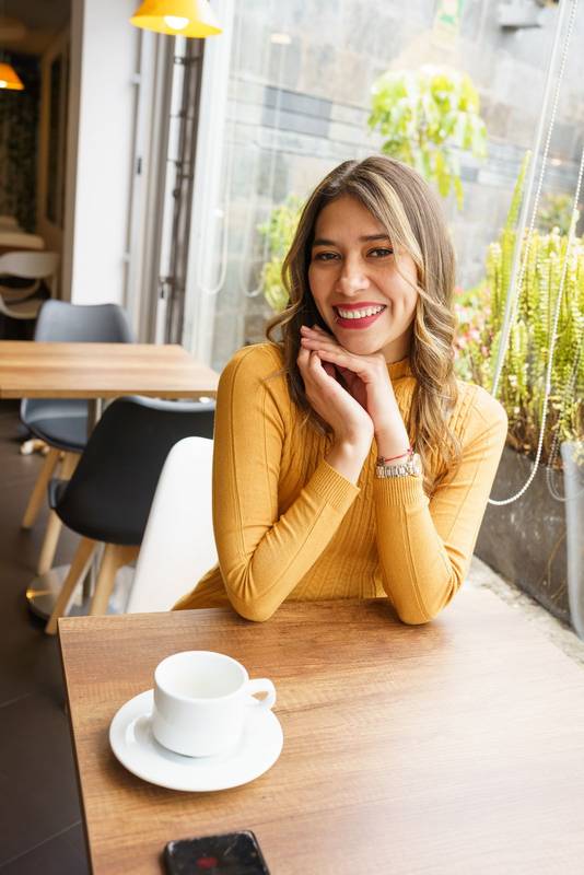 woman with wavy blonde hair, having breakfast while enjoying a hot beverage in a mug