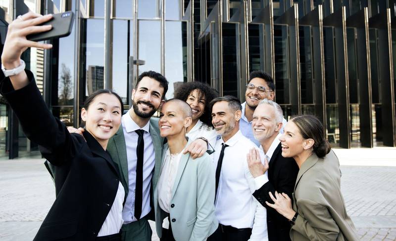 Multiracial group of cheerful and successful business people taking a selfie outside. Diverse office colleagues laughing taking a picture together smiling in the street.
