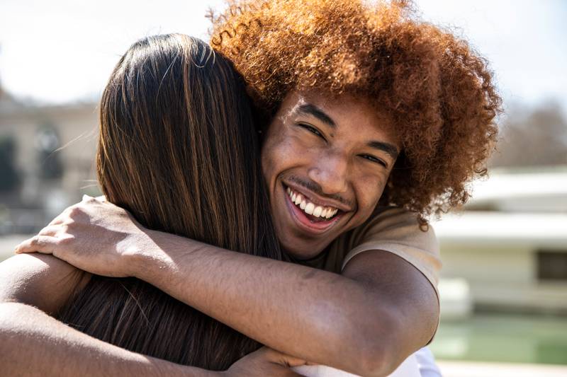 Close up of a young happy man hugging a woman with straight hair. Lovely guy smiling while embracing a lady at outdoors.