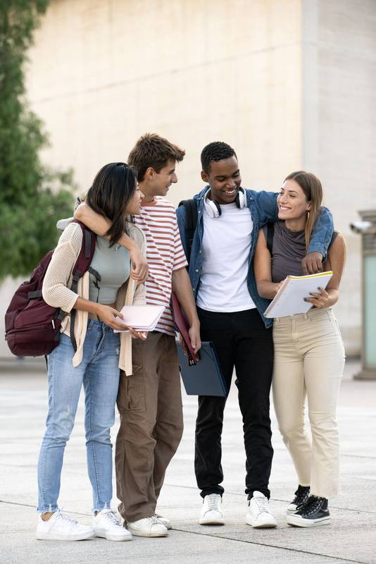 Young diverse friends walking together in embrace while reading notebooks. Joyful multiracial group of students walking hugging each other and laughing.