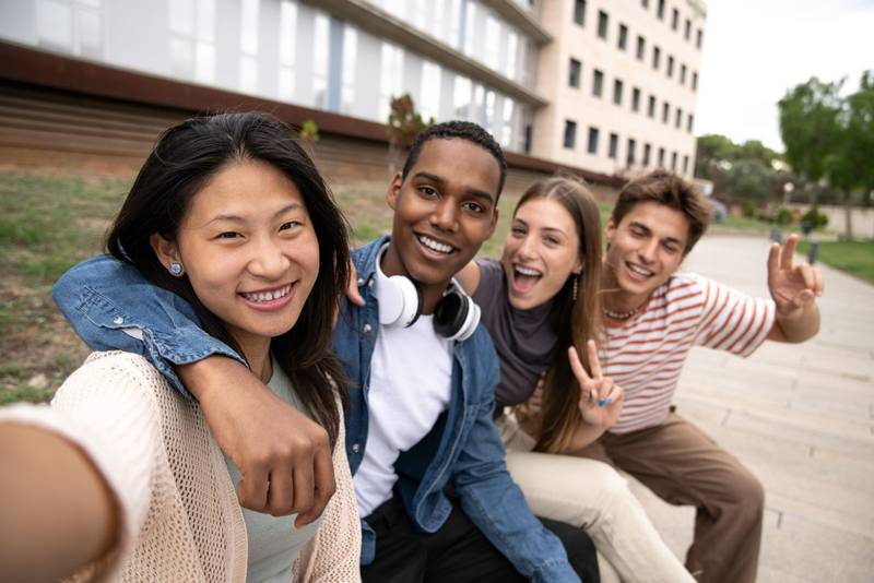 Happy joyful group of friends taking a selfie smiling. Multicultural young carefree people having fun and taking pictures outside.