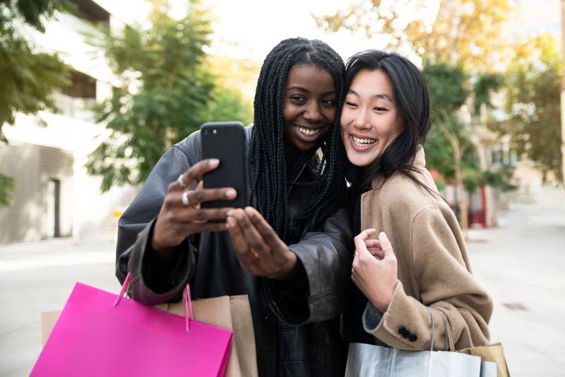 Two young beautiful smiling women making a selfie holding shopping bags - fashion concept 