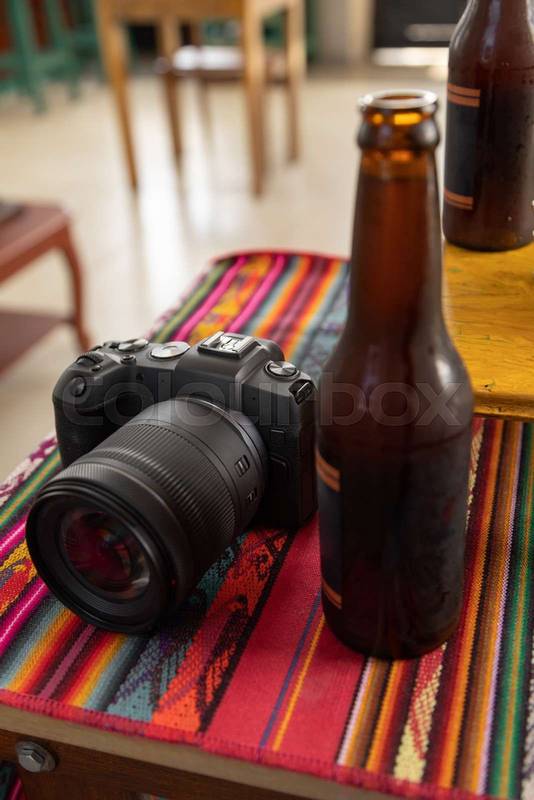 colorful tablecloth with a digital professional camera next to a bottle of beer