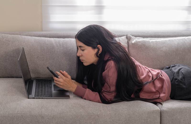 oung woman rests on her sofa at home, browsing her laptop  and cell phone