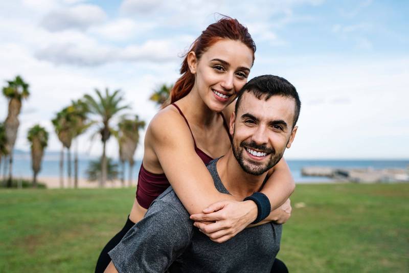 Affectionate young handsome happy fitness couple looking each other outside. Active lovely athletic boyfriend and girlfriend hugging and having fun during training.