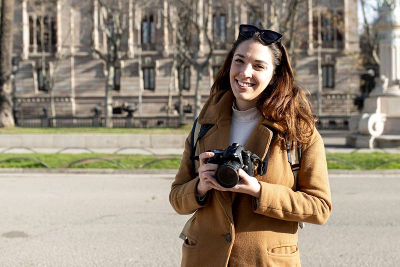 smiling woman traveler holding a camera at the city in holidays - relaxation, tourism concept