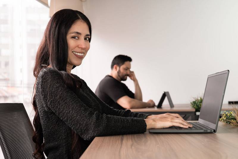 Confident woman smiles as she rests her chin on her hand while working at laptop