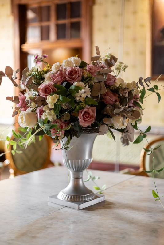 Soft pink roses and green leaves arranged in a refined silver vase