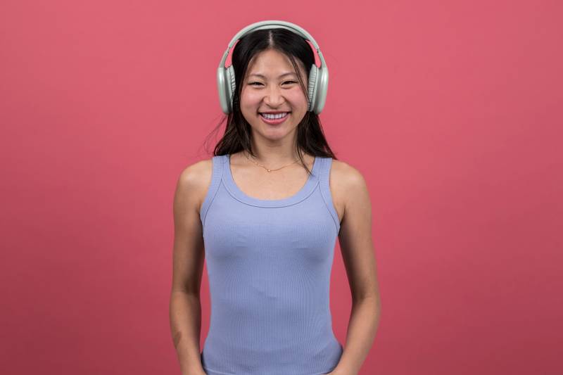 Joyful and satisfied woman with headphone looking to the camera. Smiling young female listening to music isolated on a red background.